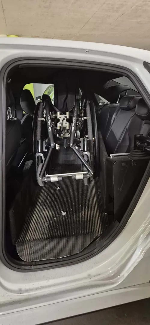 Schwarzer Rollstuhl im Kofferraum eines Autos zusammengeklappt.