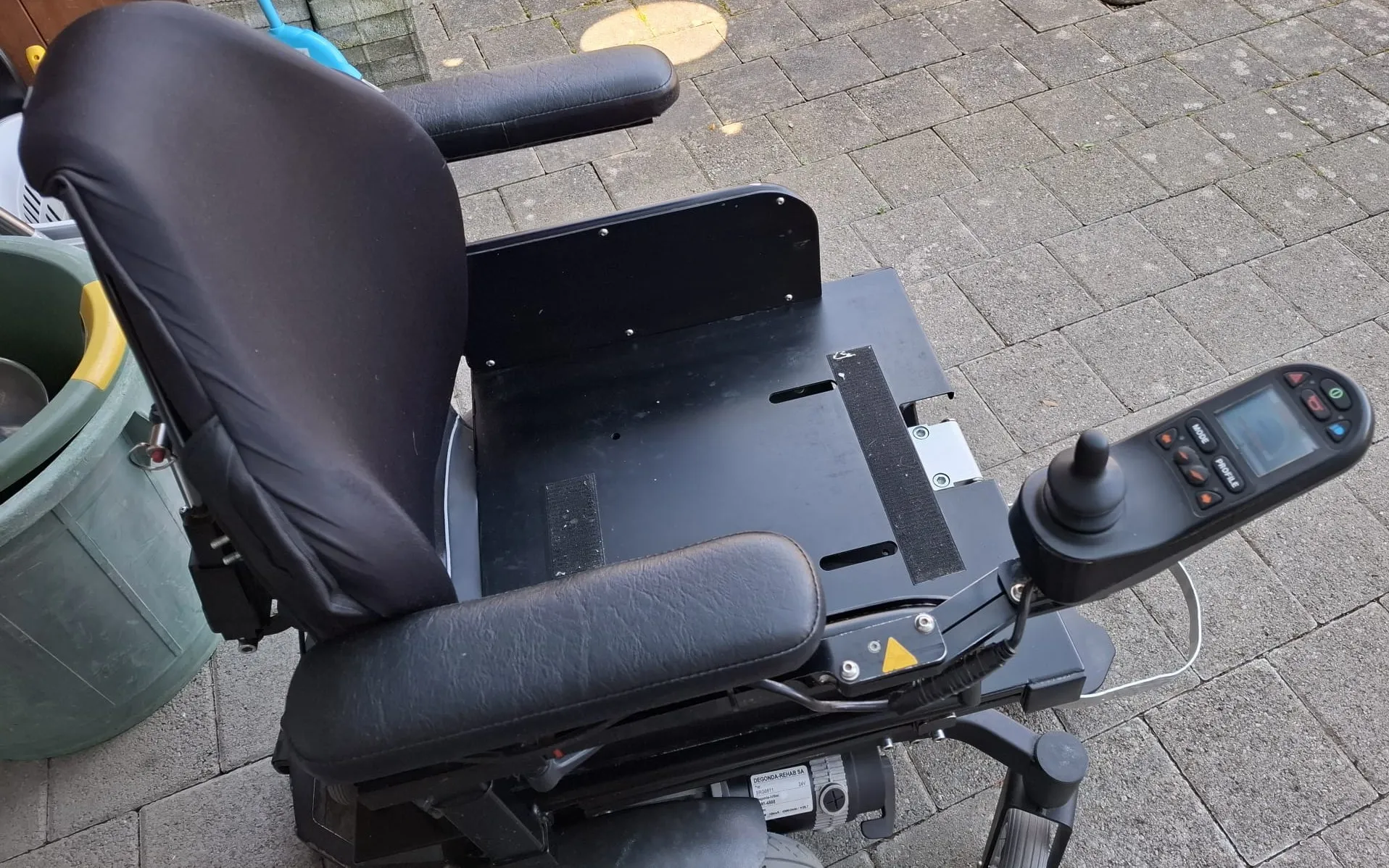 Elektrischer Rollstuhl mit schwarzem Sitz und Armlehnen auf Pflasterstein.
