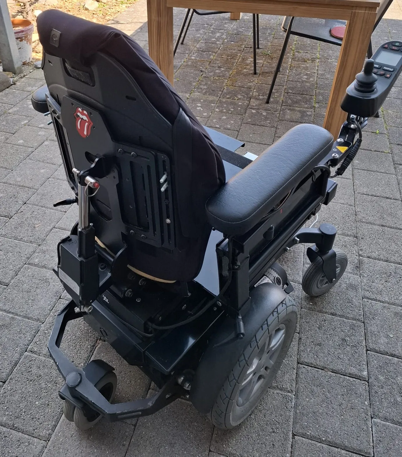 Elektrischer Rollstuhl mit schwarzem Sitz und Rückenlehne auf Pflastersteinen im Freien.