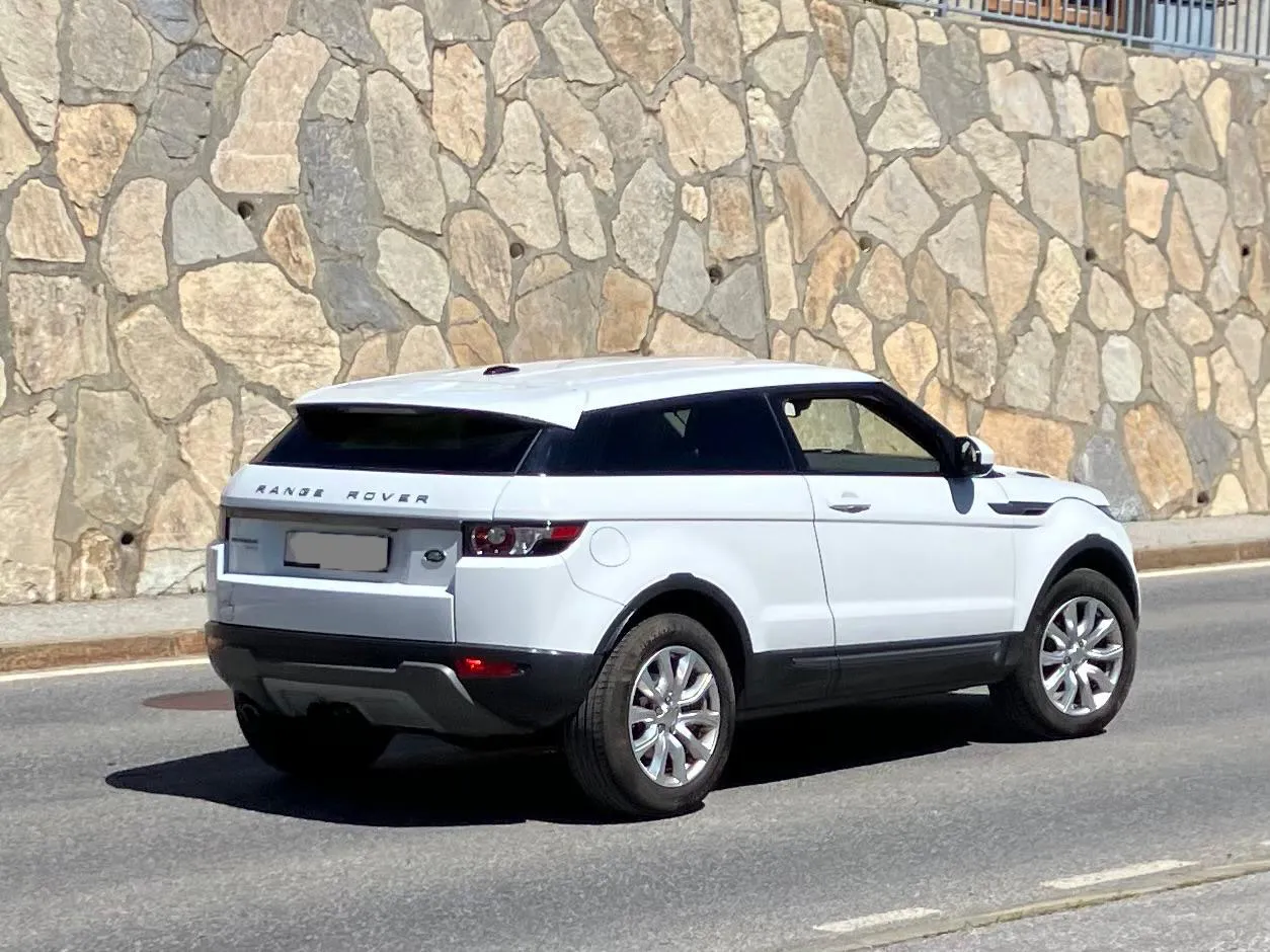 Weißer Range Rover Evoque auf Straße vor Steinmauer geparkt.
