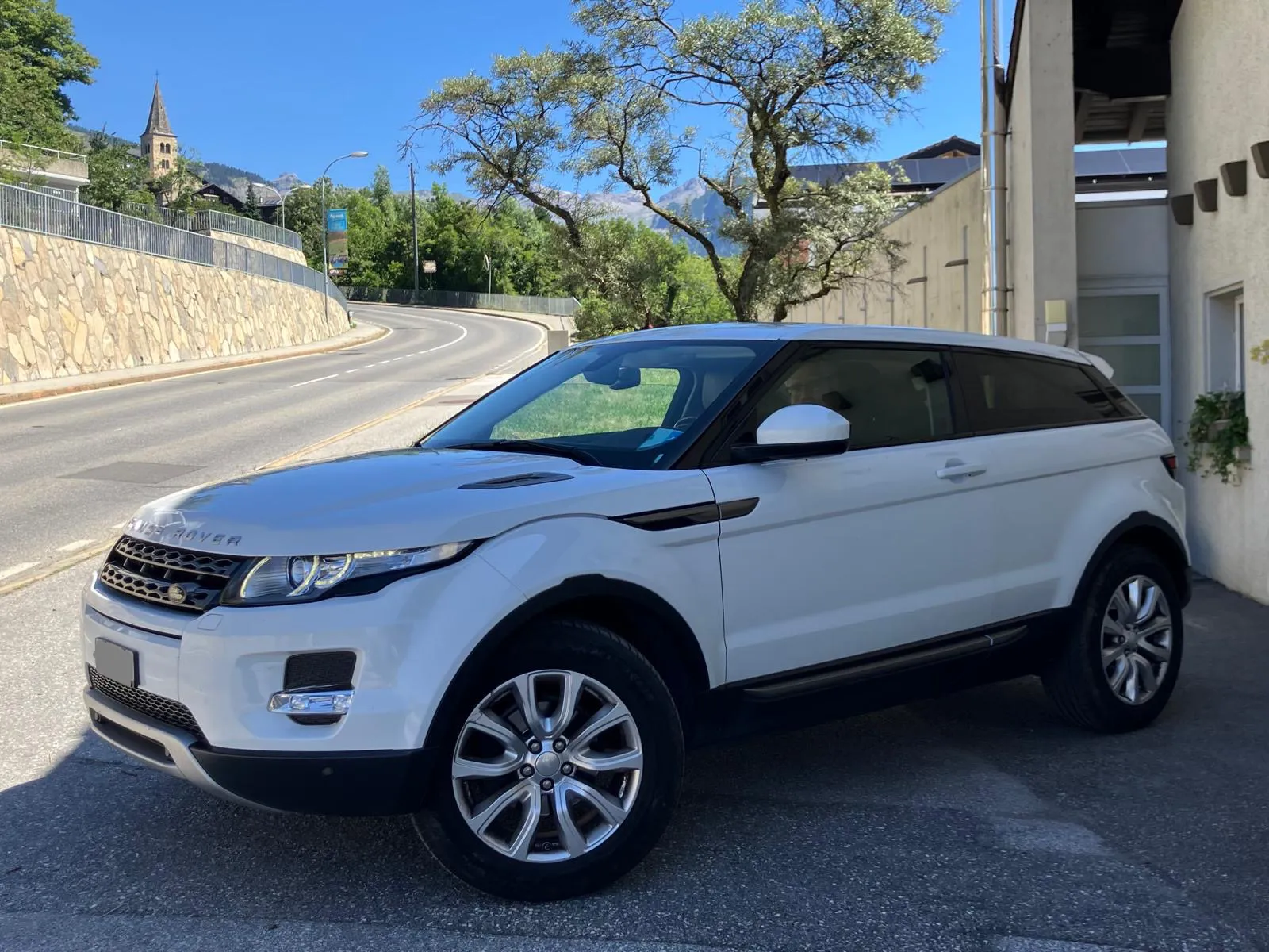 Weißer Range Rover Evoque auf gepflasterter Straße vor Steinmauer und Bäumen.