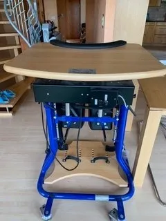 occasion-stehhilfe-schmied-08.jpg Blauer Rollstuhl mit angepasstem Holztisch für ergonomisches Arbeiten.