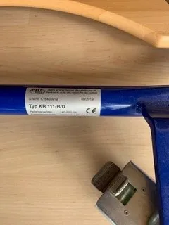occasion-stehhilfe-schmied-10.jpg Blauer Rollstuhl mit Seriennummer auf Etikett, Holztisch im Vordergrund.