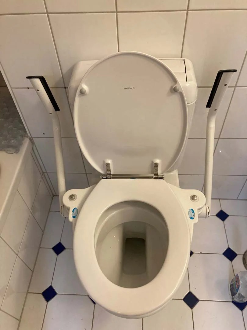 occasion-toilettensitzerhoehung-th-10-messerli-01.jpg Toilettensitz mit Haltegriffen in einer öffentlichen Toilette.