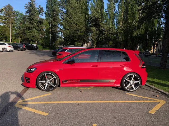 Roter Volkswagen Golf GTI parkt auf gelbem Parkplatz neben Bäumen.