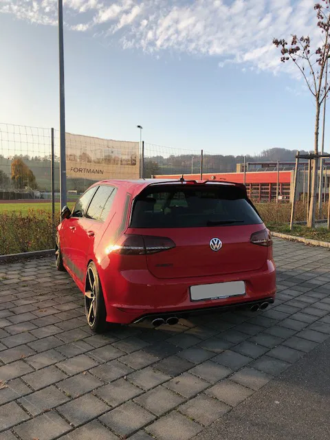 Roter Volkswagen Golf auf gepflastertem Parkplatz bei Sonnenuntergang.