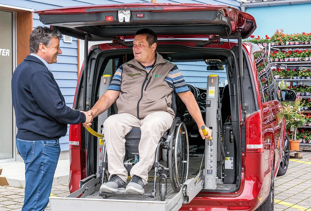 Daniel Brem ist mit seinem Rollstuhl im Kofferraum seines Autos und schüttelt einer Person die Hand.