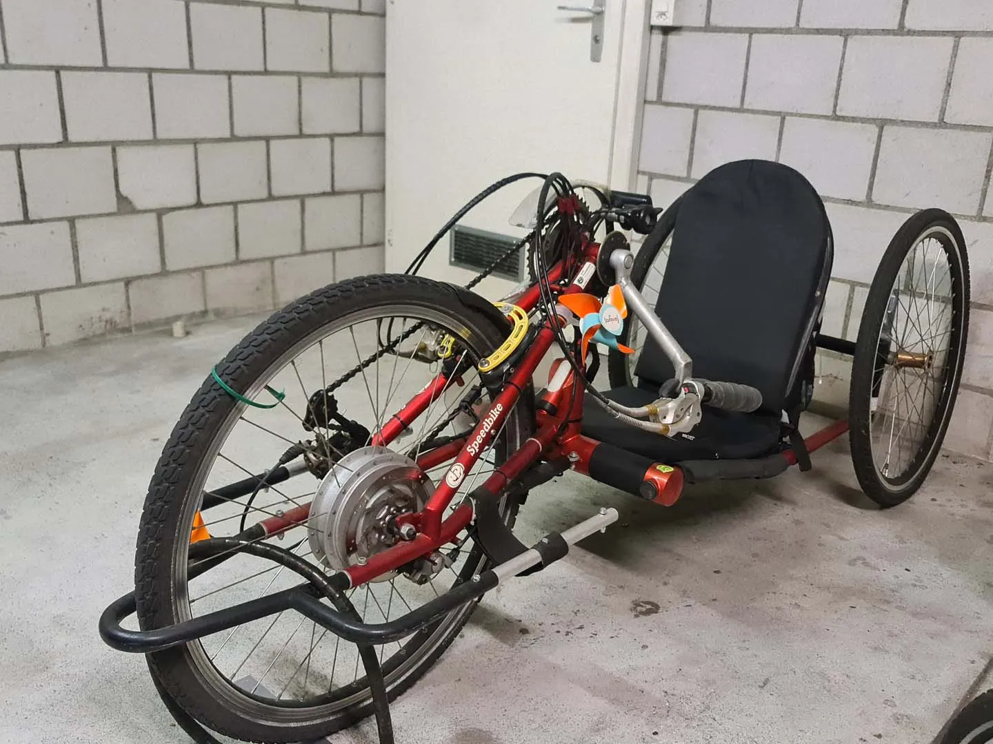 occasion-speedbike-nguyen-01.jpg Rotes Handbike mit drei Rädern in einem gefliesten Raum geparkt.