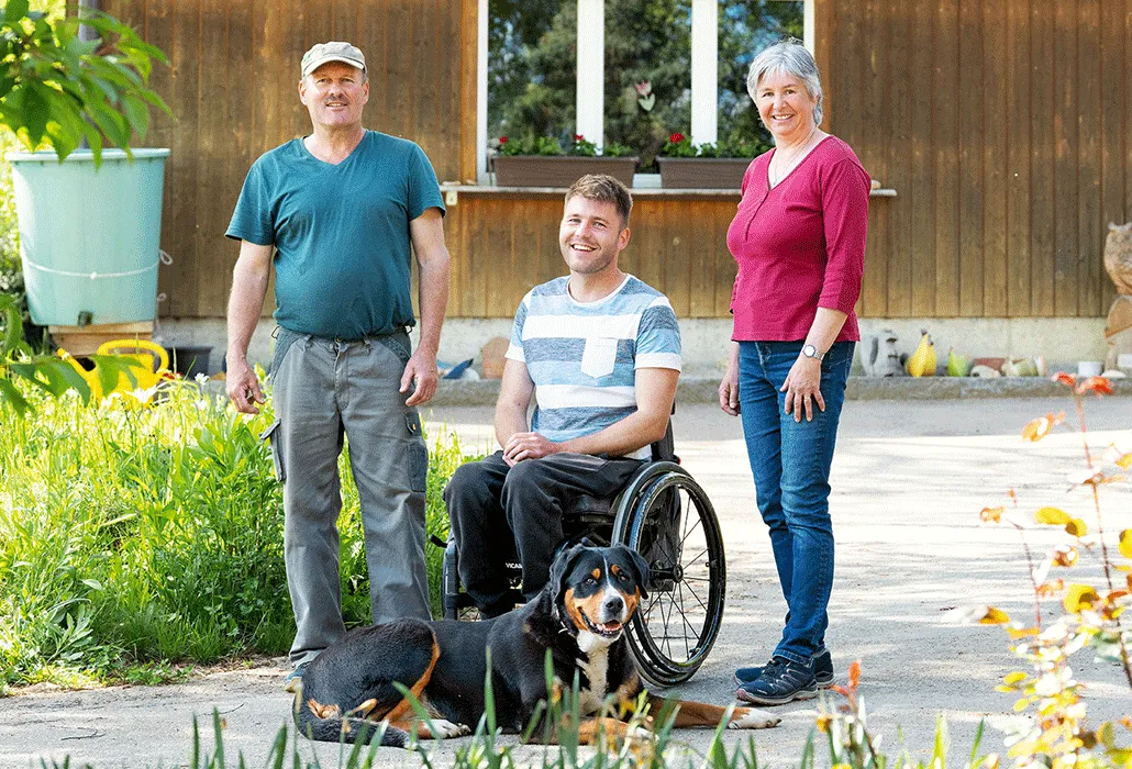 Markus Buser ist zusammen mit seinen Eltern vor dem Hof. Der Hund liegt vor ihnen auf dem Boden.