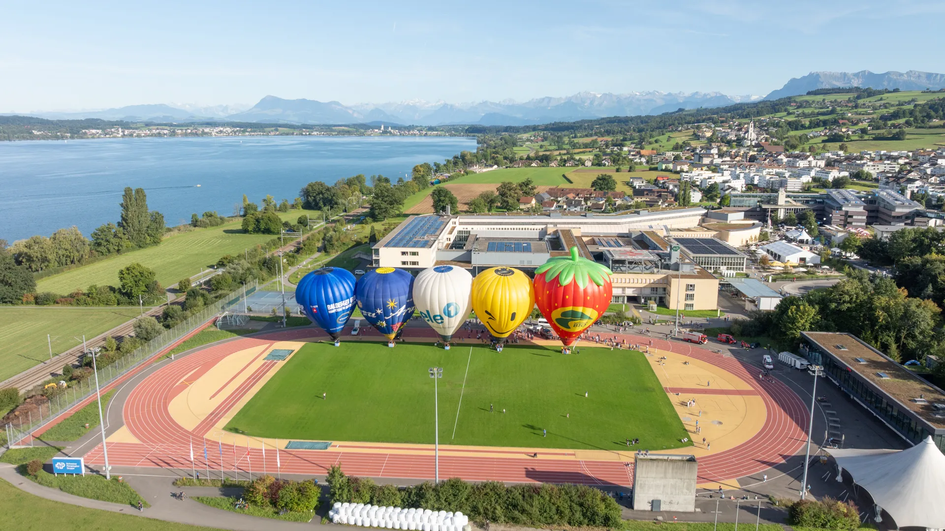 Vier Heissluftballone auf dem Sportplatz der Schweizer Paraplegiker-Gruppe, aus der Luft fotografiert..
