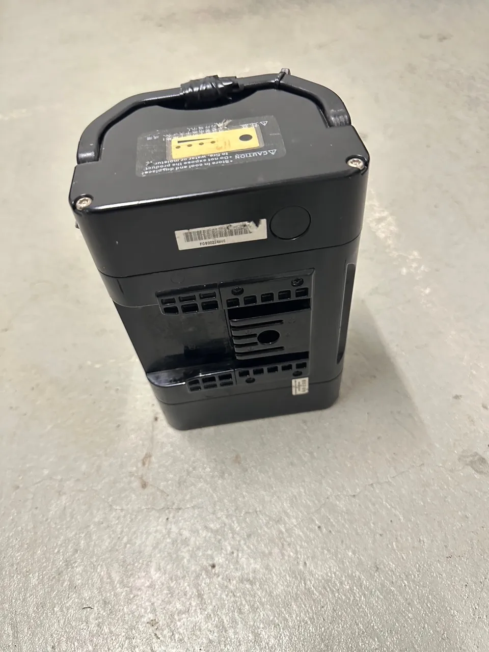 occasion-batterien-stricker-klaeger-05.jpg Schwarzes elektronisches Gerät mit gelben Akzenten auf grauem Stoff.