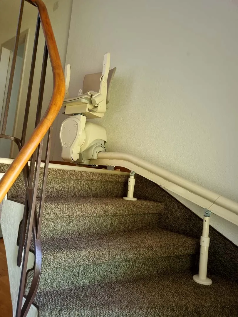 occasion-hoegg-sitzlift-kueffer01.jpg Gebogener Treppenlift auf schmaler Treppe mit Teppichbelag und Holzgeländer.