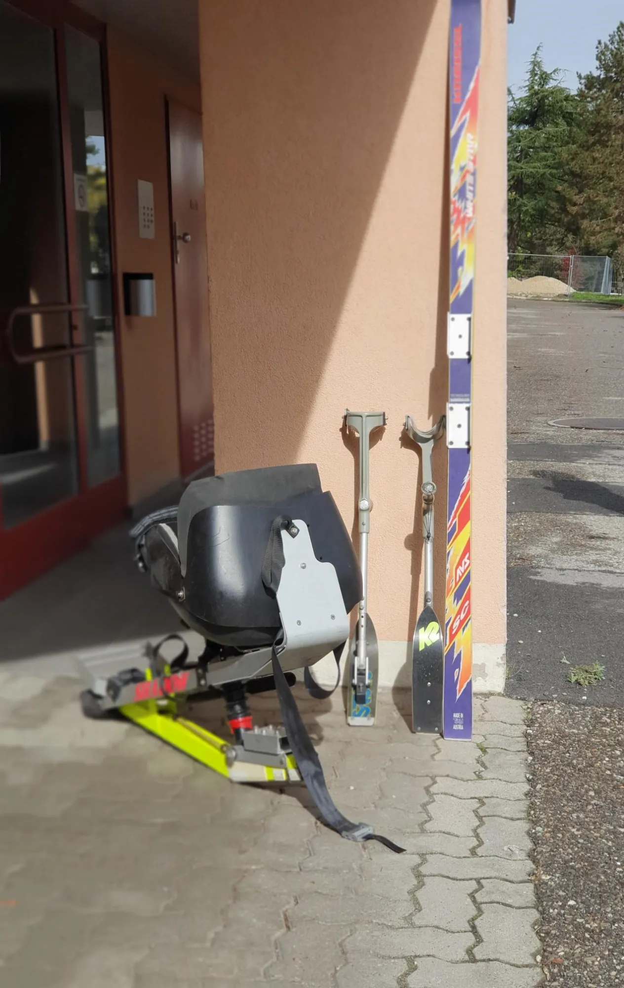 occasion-quickie-skibob-torny-02.jpg Grauer Roller vor einem Geschäftseingang mit Regenbogenfarben und Skateboard.