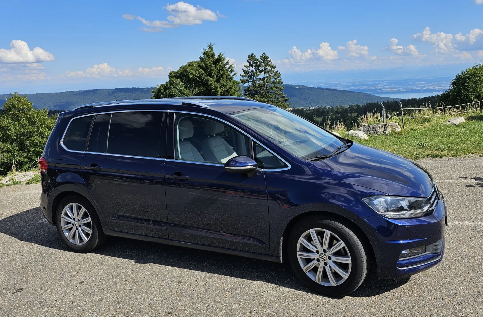 Dunkelblauer Minivan auf einer Bergstraße mit Meerblick im Hintergrund.