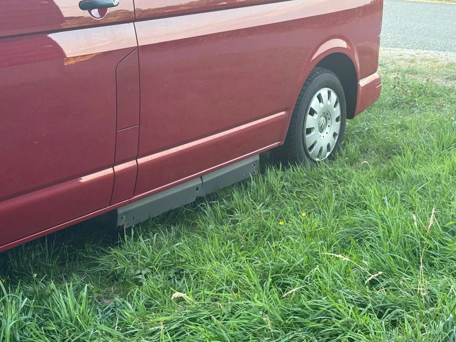 Seitentür und Rad eines burgunderroten Vans auf grünem Gras
