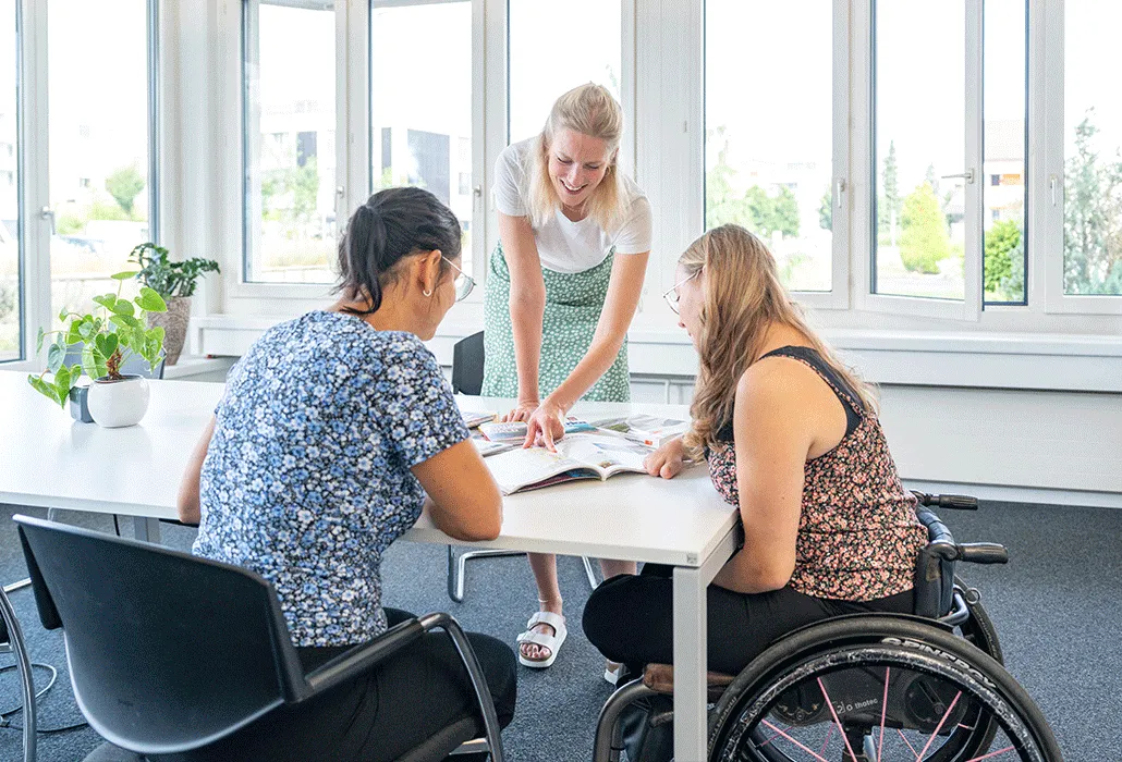 Drei Frauen sitzen um einen Tisch herum und beugen sich über Magazine.