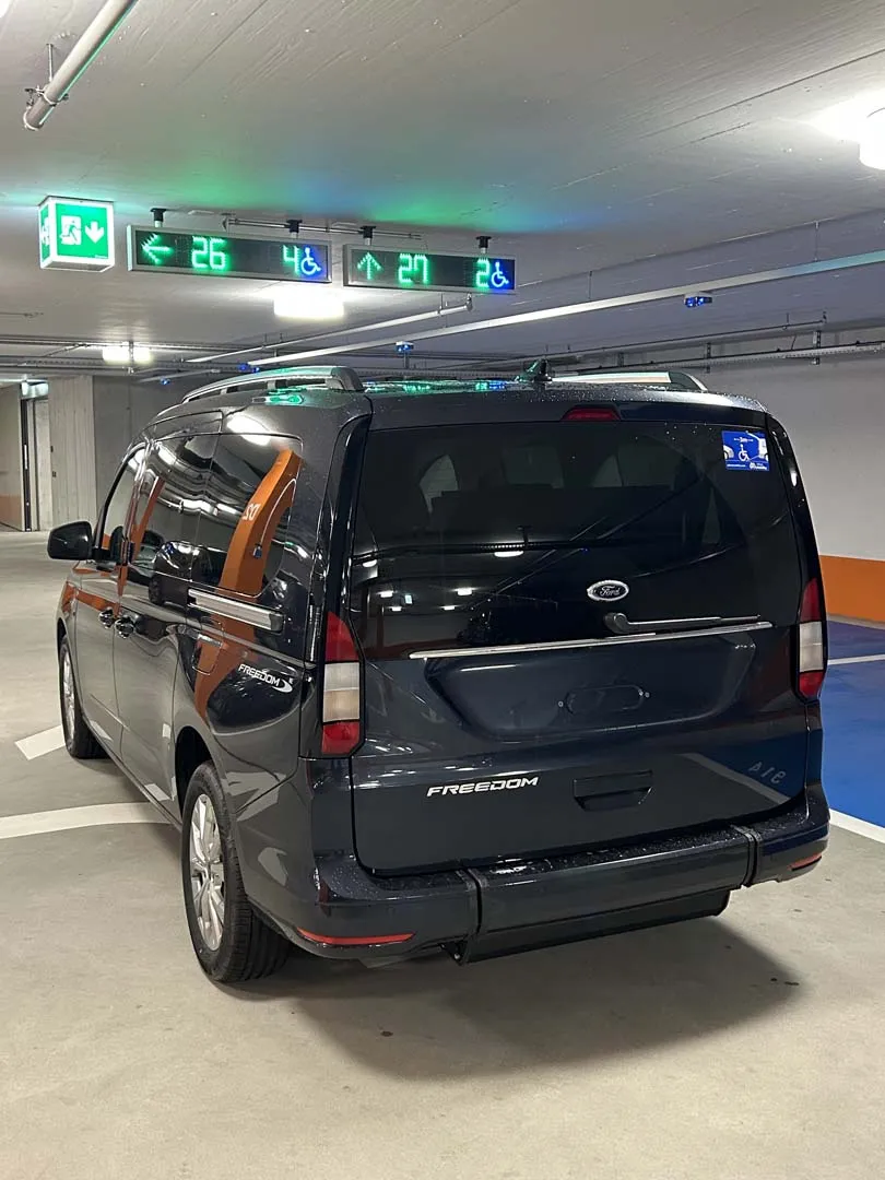 occasion-ford-tourneo-connect-blau-orthotec-02.jpg Dunkelblaues Familienauto in Tiefgarage mit grünen Ausfahrtschildern an der Decke.