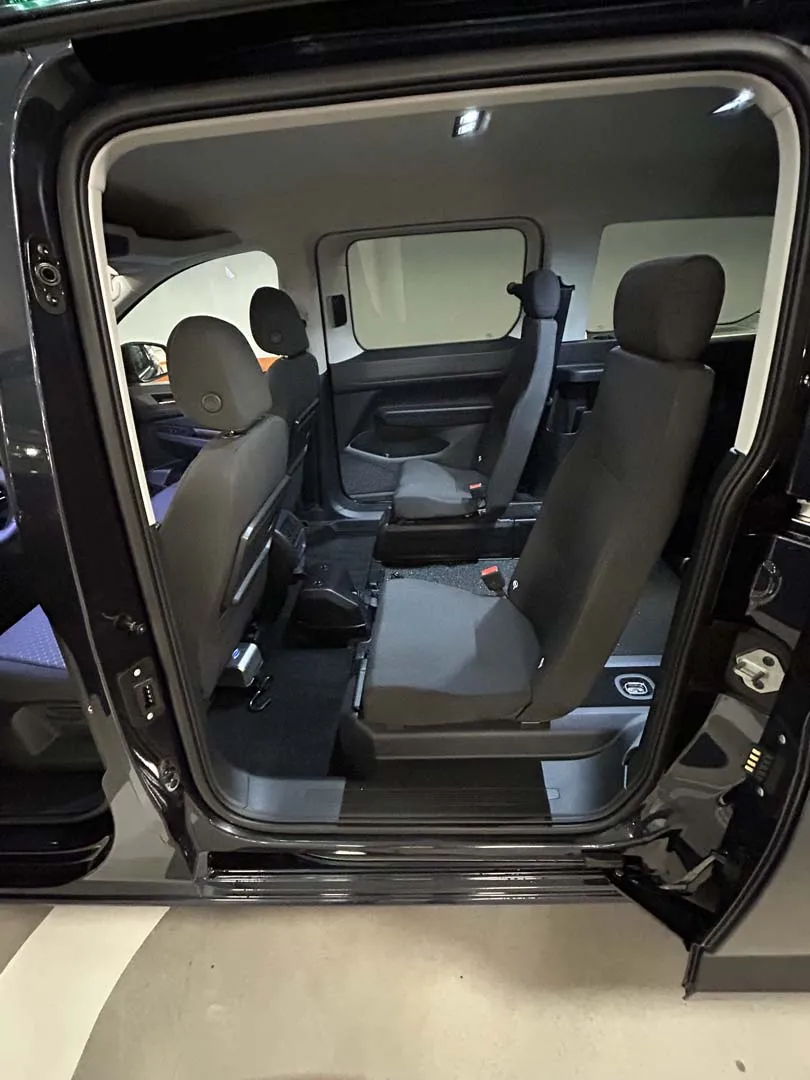 occasion-ford-tourneo-connect-blau-orthotec-08.jpg Innenraum eines Vans mit geöffneter Seitentür, schwarze Ledersitze und helle Deckenbeleuchtung.
