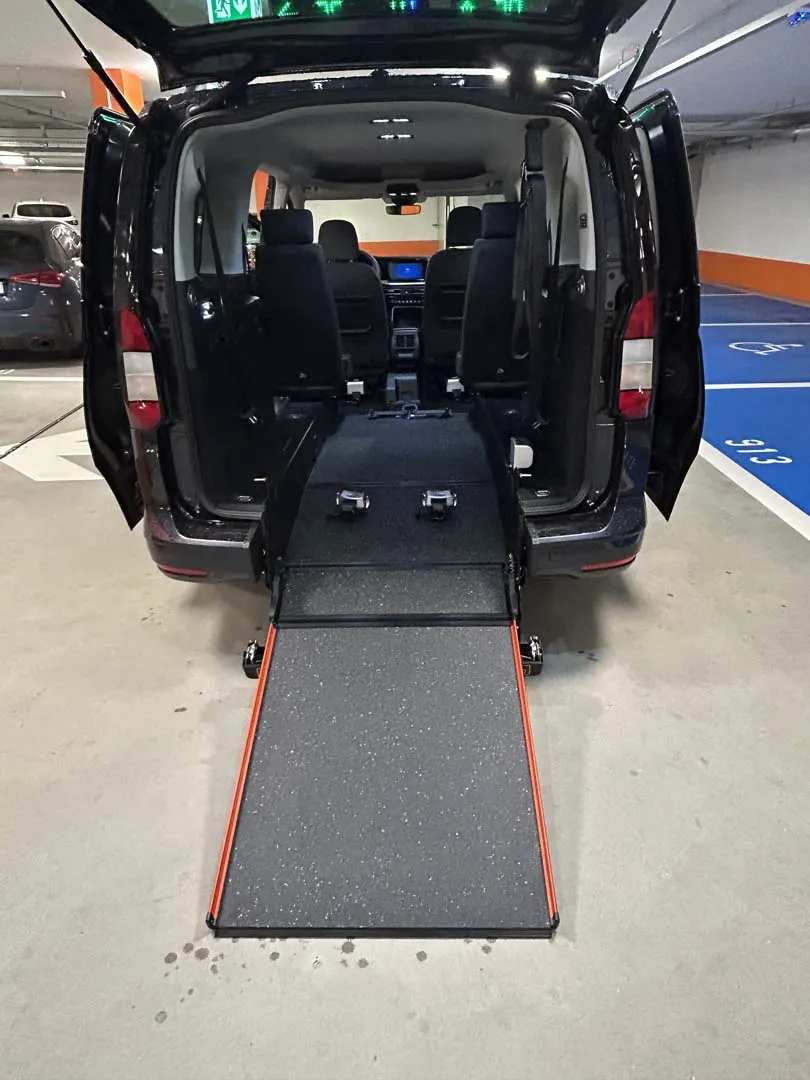 occasion-ford-tourneo-connect-blau-orthotec-09.jpg Behindertengerechtes Fahrzeug mit ausgefahrener Rampe für Rollstuhlzugang im Innenraum.