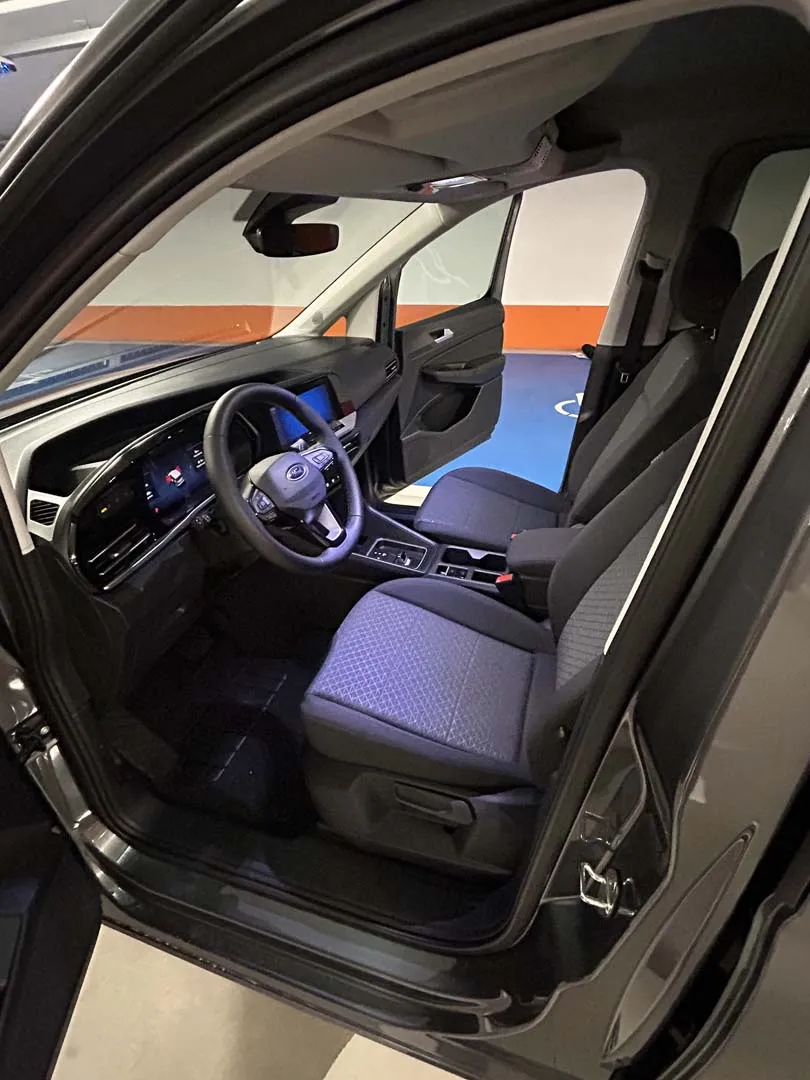 occasion-ford-tourneo-connect-grau-orthotec-07.jpg Innenraum eines Autos mit blauer Beleuchtung, offene Fahrertür und Lenkrad sichtbar.
