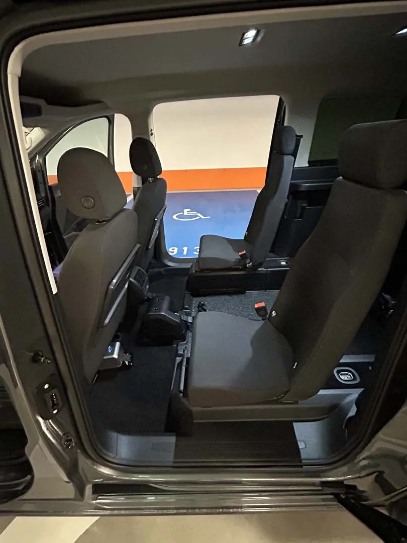 occasion-ford-tourneo-connect-grau-orthotec-08.jpg Innenraum eines Fahrzeugs mit schwarzen Sitzen und Sicherheitsgurten, offene Tür zeigt Sonnenuntergang.