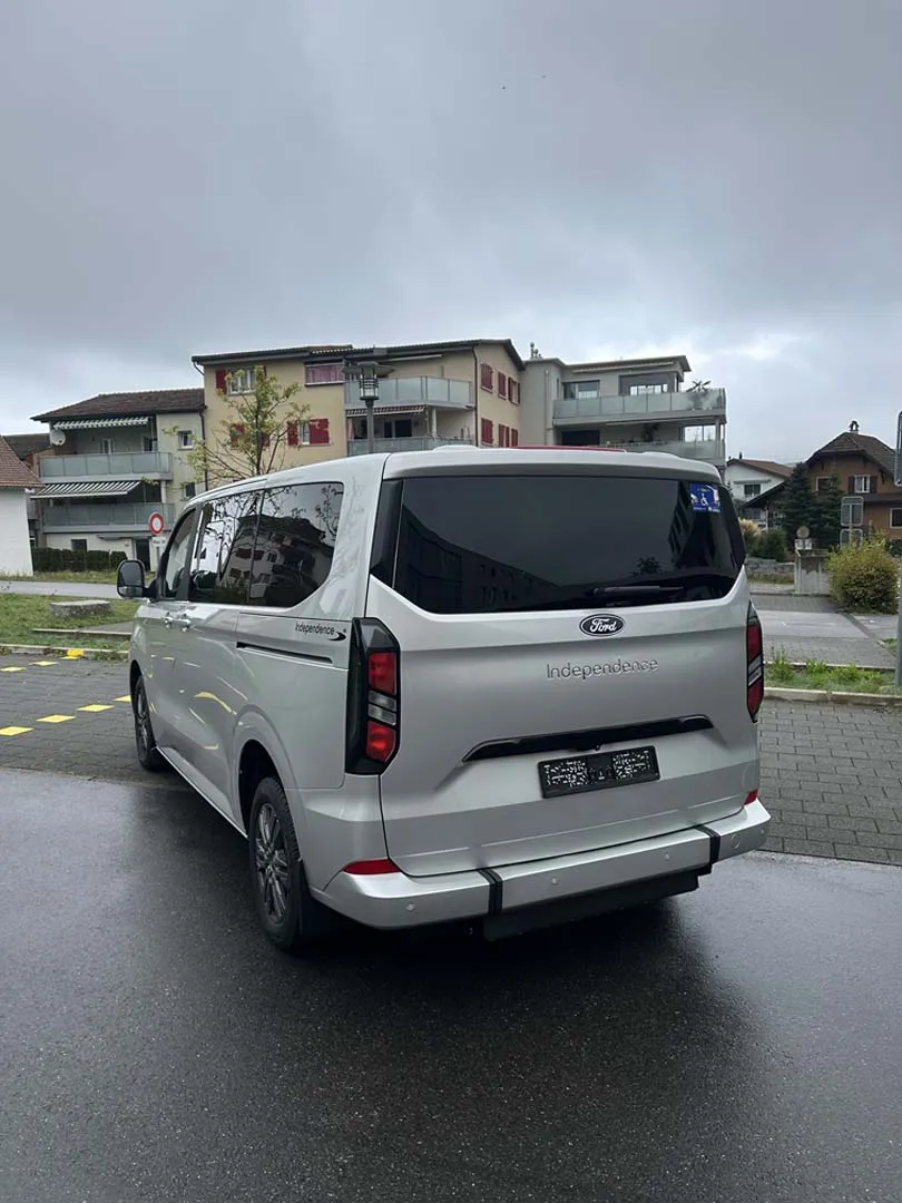 occasion-ford-tourneo-connect-silber-orthotec-02.jpg Weißer Minivan parkt vor Wohnhäusern an einer Straße bei bewölktem Himmel.