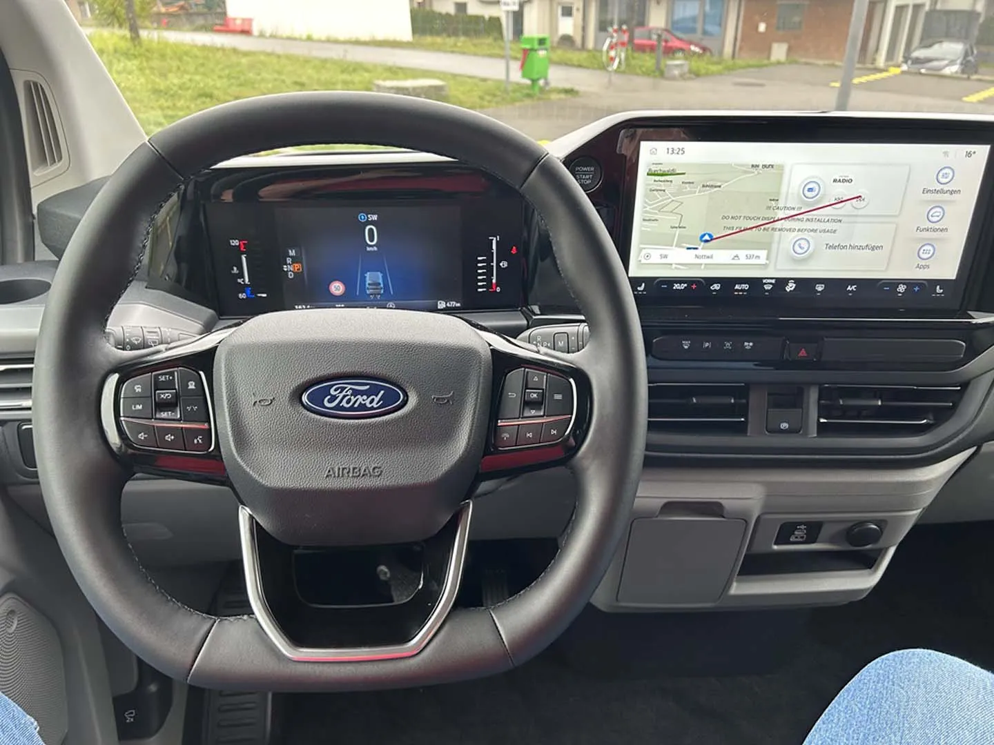 occasion-ford-tourneo-connect-silber-orthotec-05.jpg Lenkrad und Armaturenbrett eines modernen Ford-Fahrzeugs mit großem Touchscreen-Display.