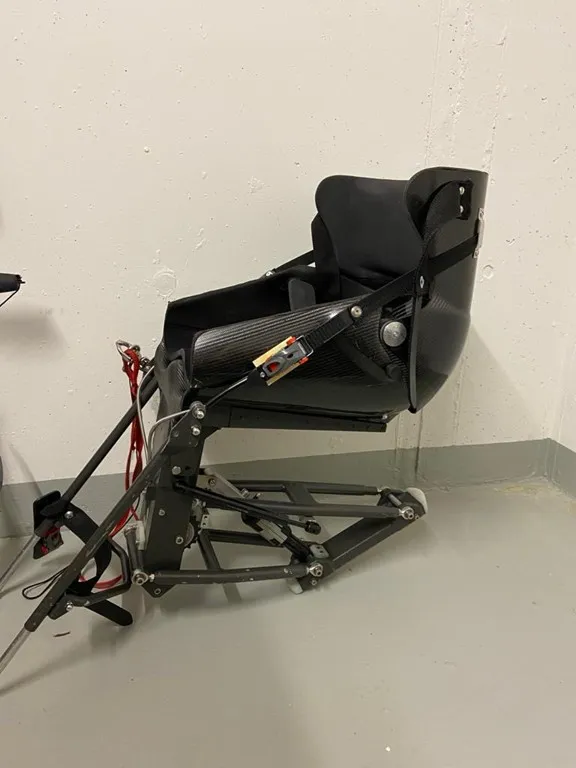 occasion-nolimit-monoskibob-sonderer-01.jpg Rollator und Rollstuhl neben einem schwarzen Sessel in einem schlichten Raum.