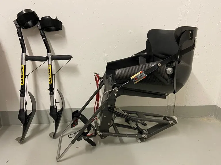 occasion-nolimit-monoskibob-sonderer-02.jpg Schwarzer Bürostuhl und zwei Elektro-Scooter an einer hellen Wand lehnend.
