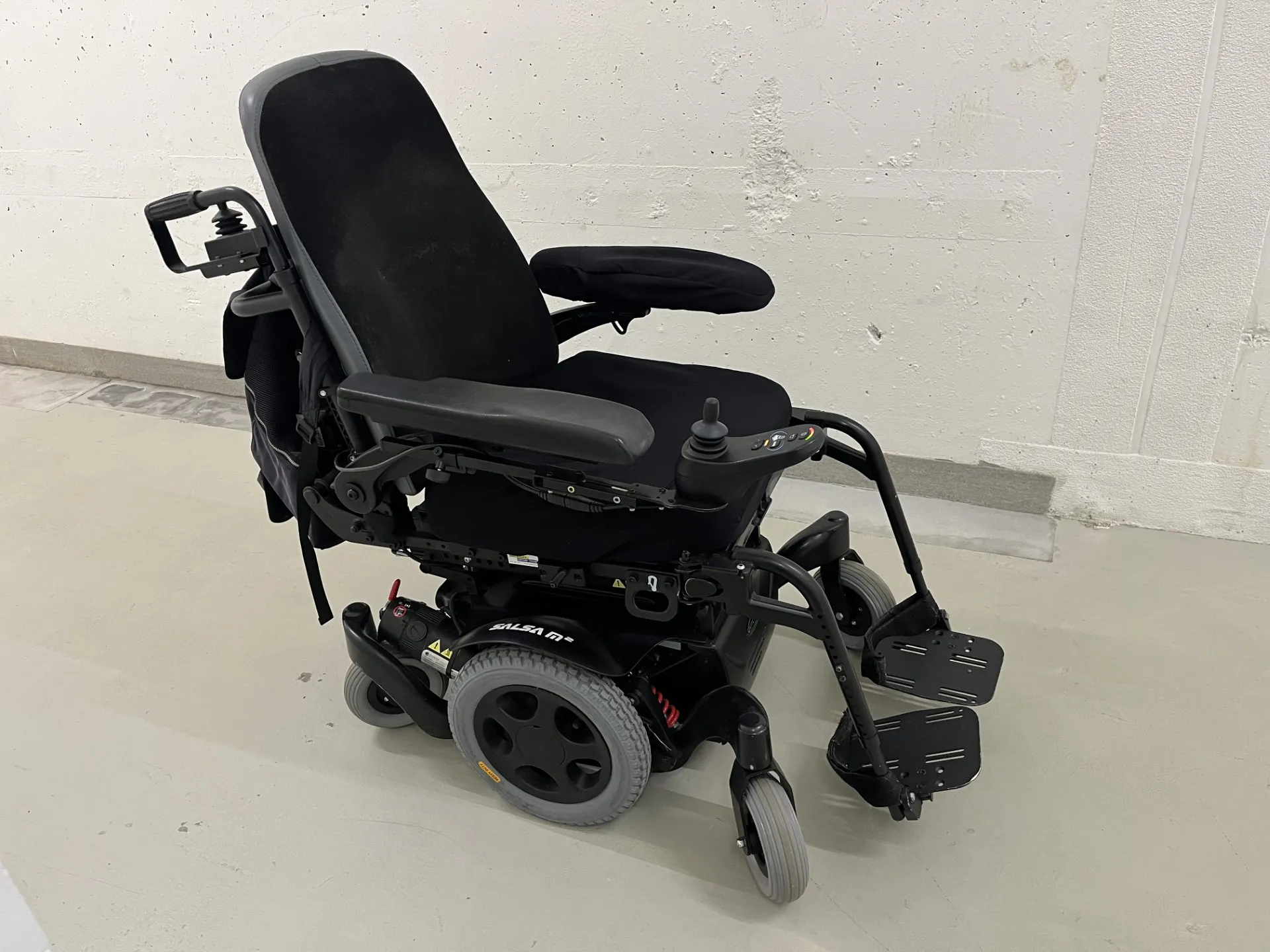 Schwarzer elektrischer Rollstuhl mit verstellbarer Rückenlehne und Fußstützen auf weißem Boden.