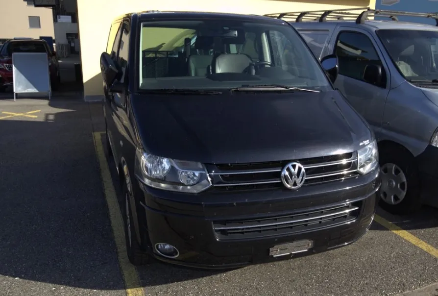 Schwarzer VW Transporter T6 geparkt auf Asphalt vor Gebäude
