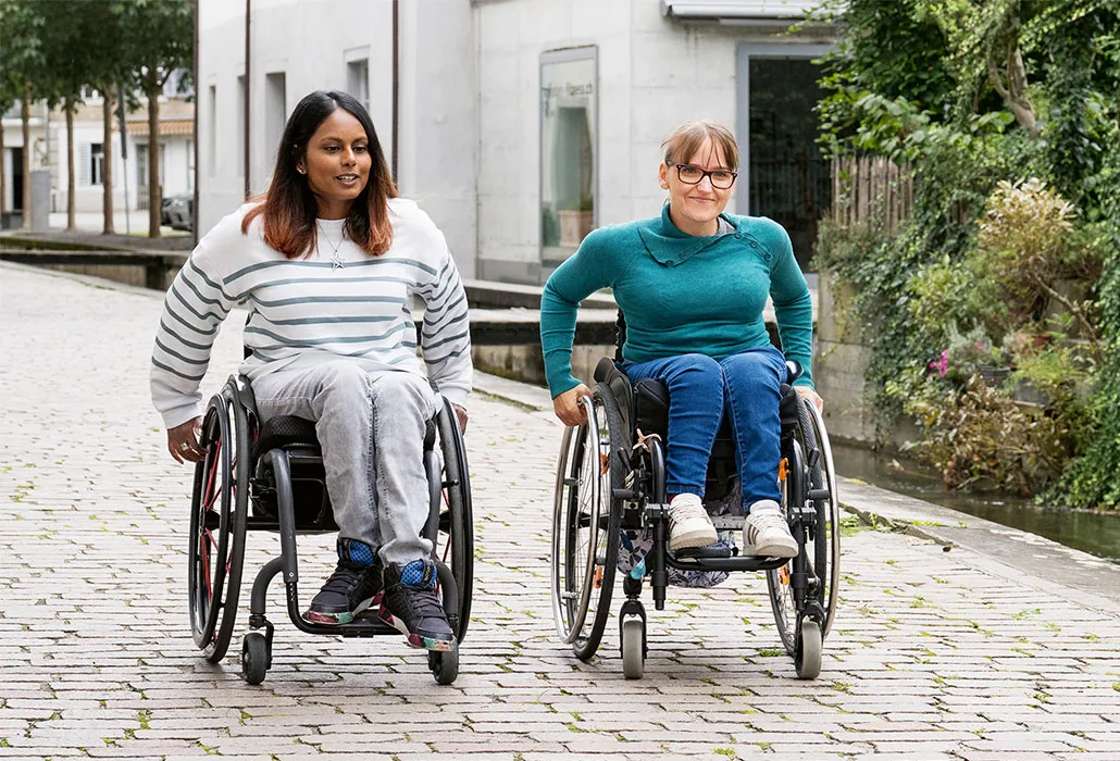 Alexandra Helbling und eine Freundin von ihr fahren gemeinsam im Rollstuhl über Pflasterstein in der Stadt.