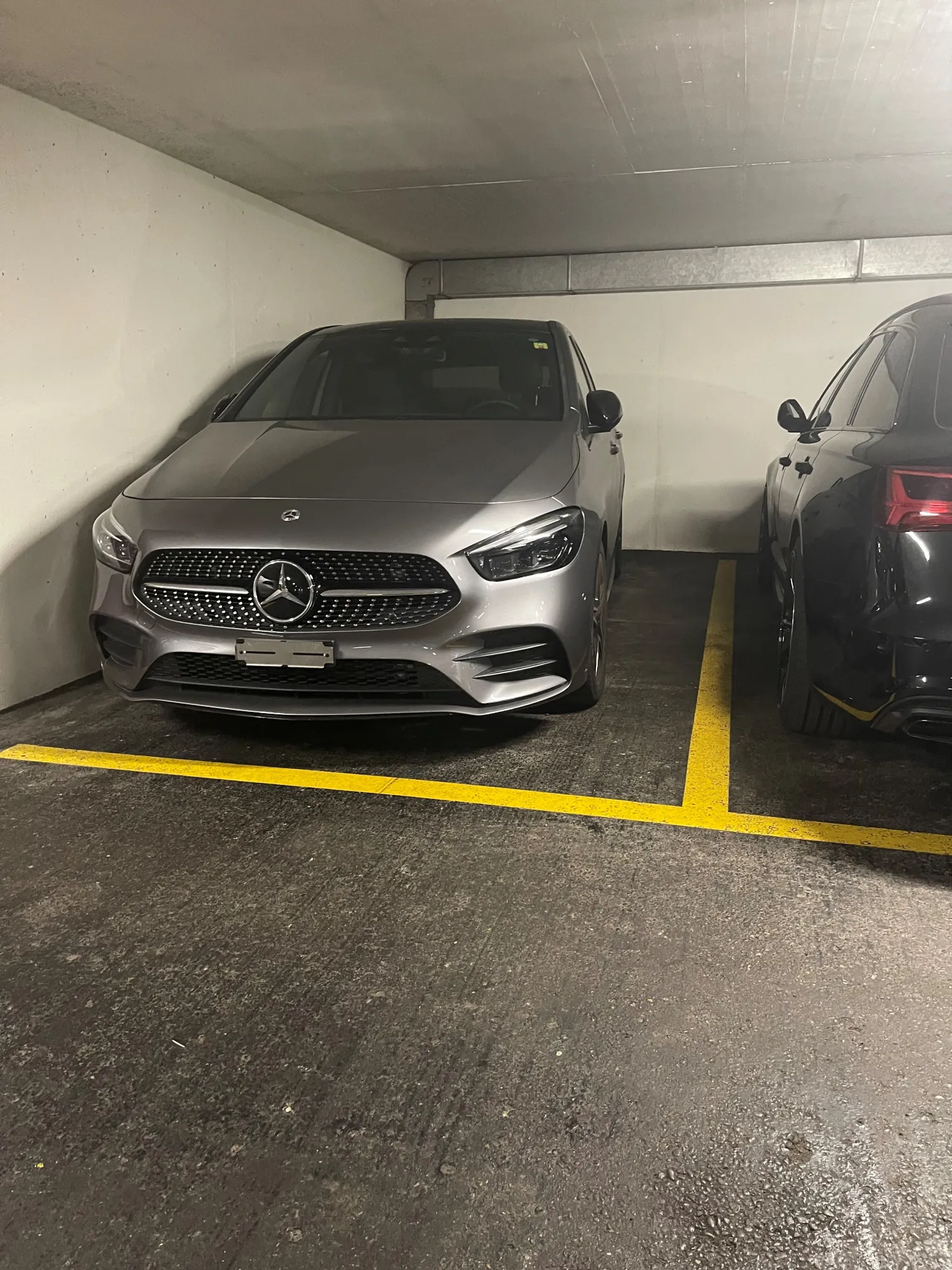 Zwei silberne Mercedes-Benz Autos in einer Tiefgarage auf markierten Parkplätzen.