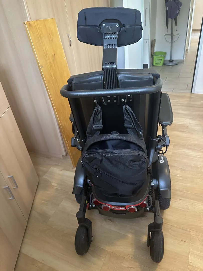 Elektrischer Rollstuhl mit schwarzem Sitz und gelber Rampe im Hintergrund.