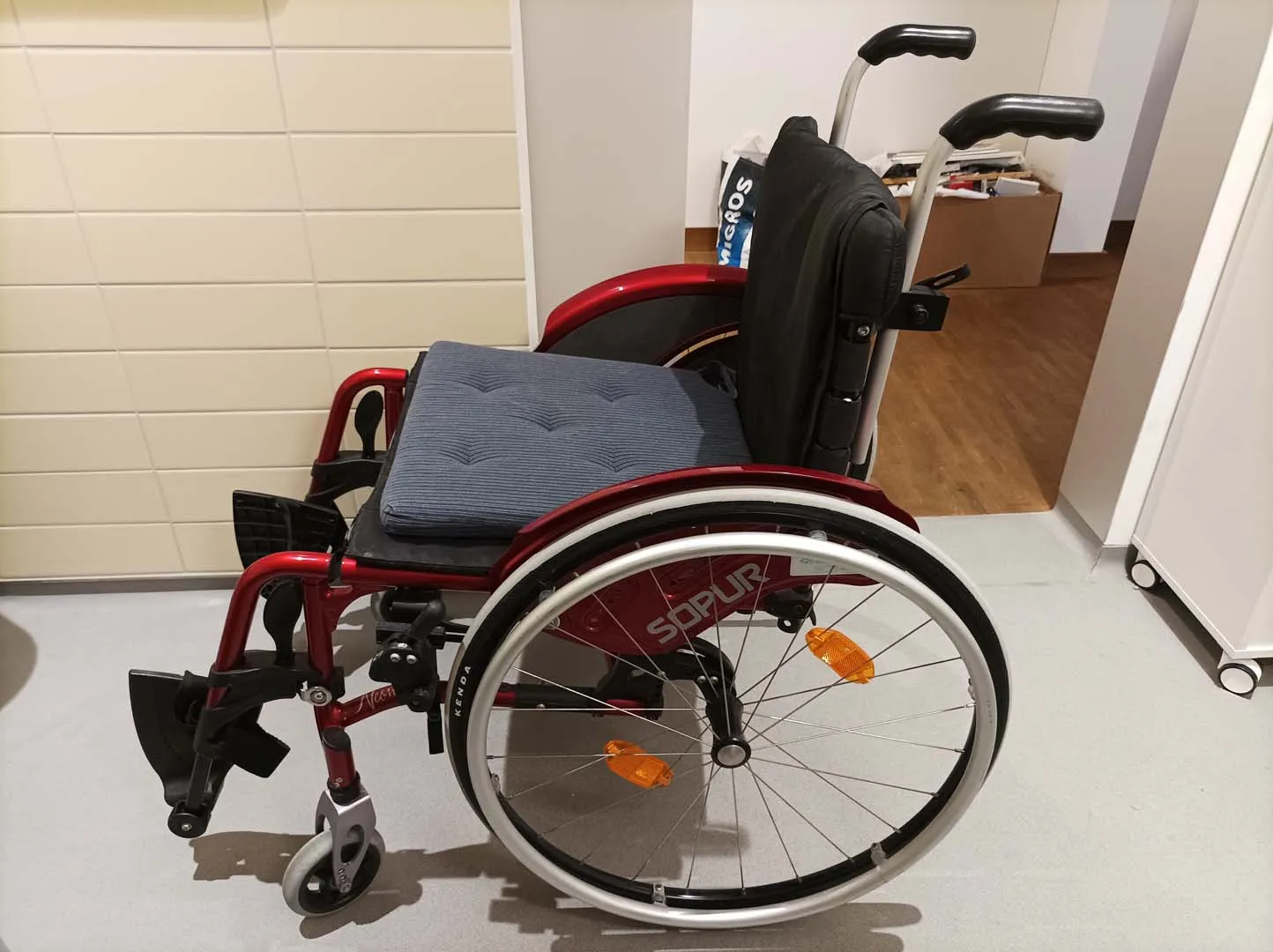 Roter Rollstuhl in einem Flur mit beiger Wand und Holzboden.