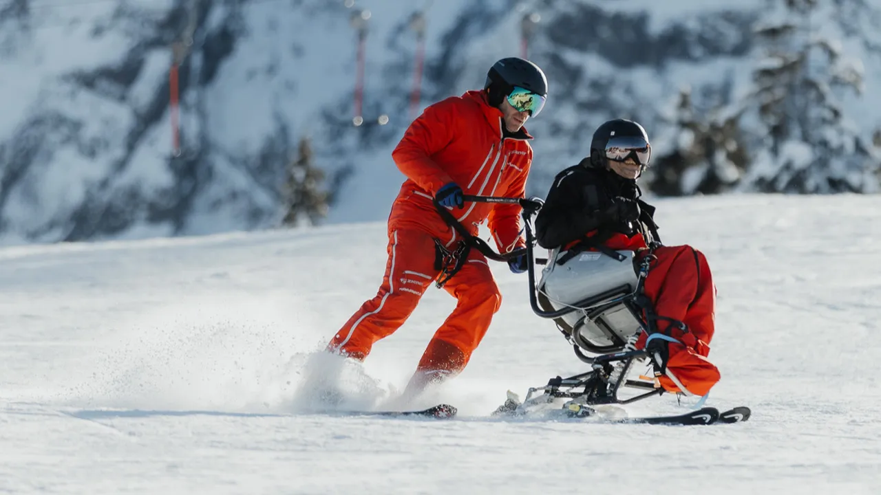 Monoskibob Fahrender wird von einem Skilehrer geführt.