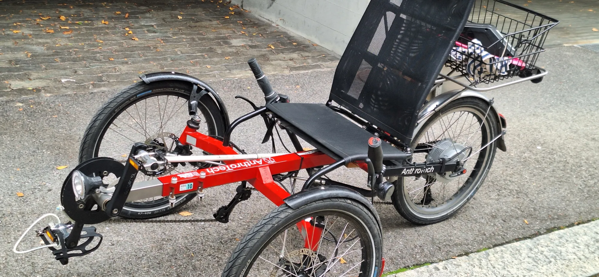 occasion-dreirad-merz.jpg Rotes Liegerad mit drei Rädern auf Betonboden geparkt.