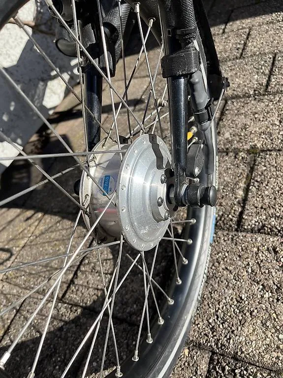 occasion-hasebike-ammann-02.jpg Nahaufnahme eines Fahrrad-Vorderrads mit Nabendynamo auf Kopfsteinpflaster