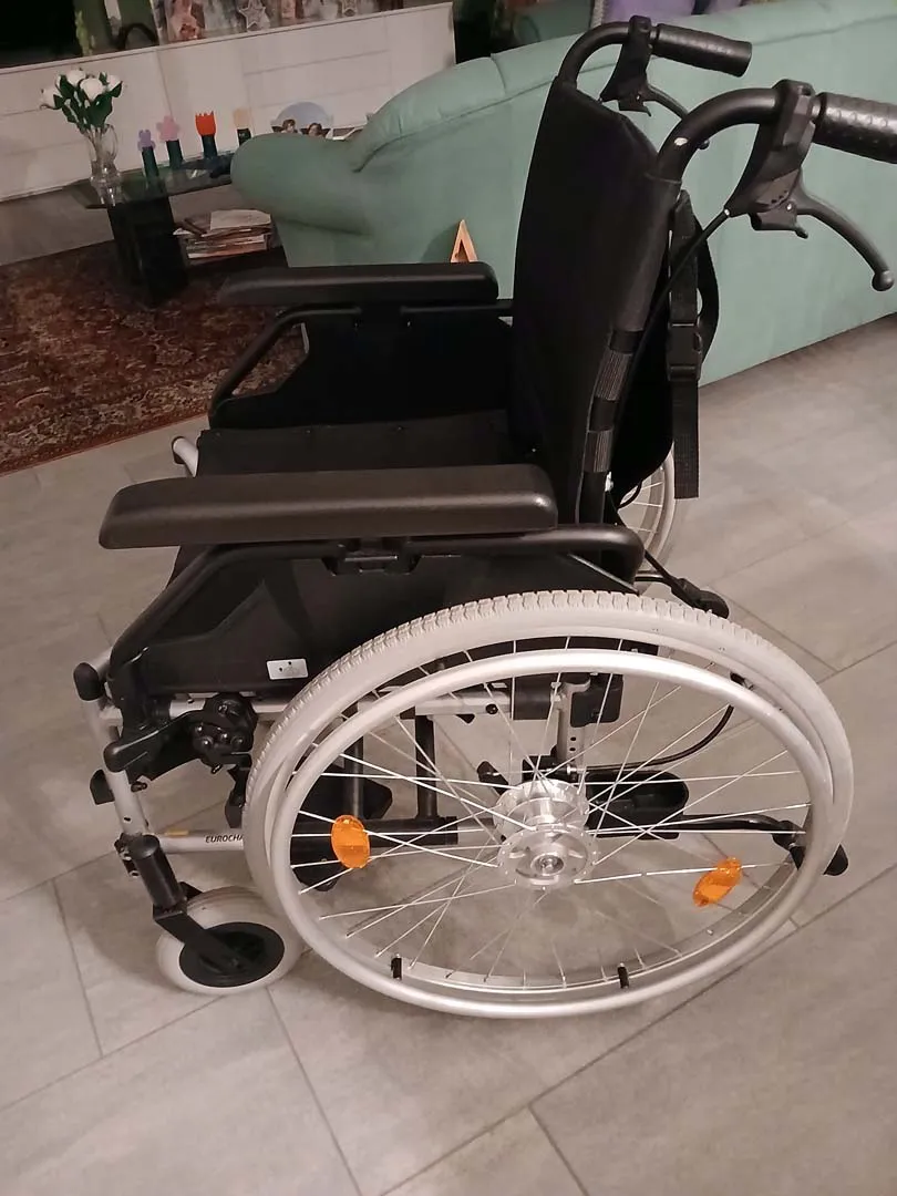 Leerer Rollstuhl mit grauem Rahmen und großen weißen Rädern auf Fliesenboden.