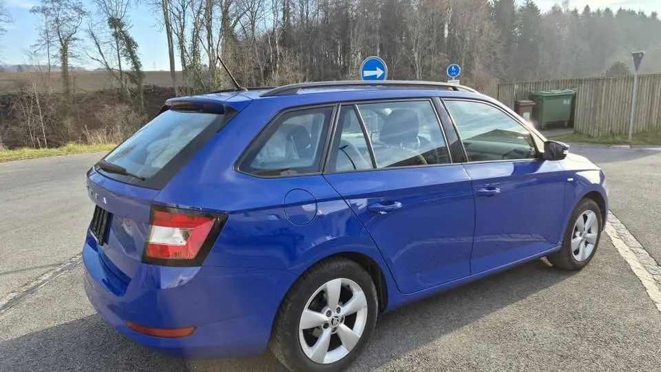 Blauer Skoda Fabia Kombi auf Parkplatz, umgeben von Bäumen.