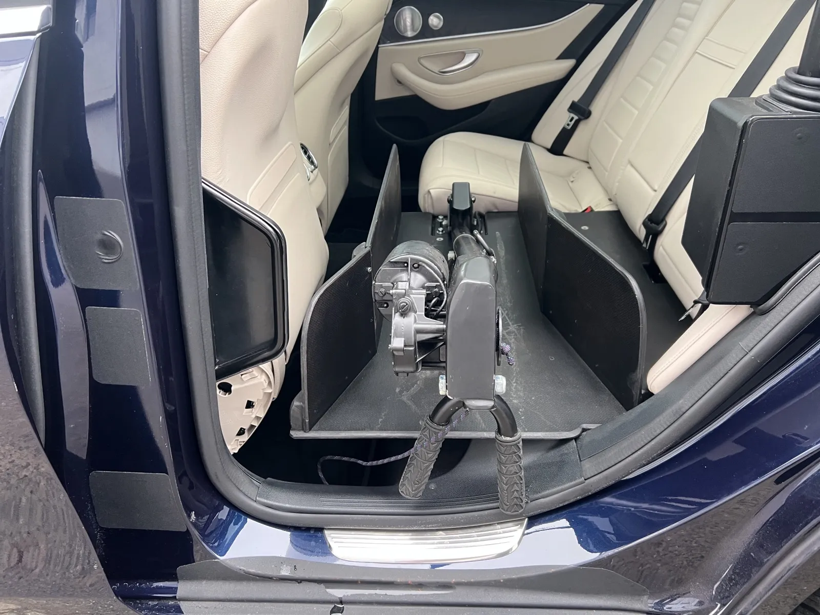 Hund sitzt angeschnallt auf einer Autositzabdeckung im Rücksitz eines blauen Fahrzeugs.