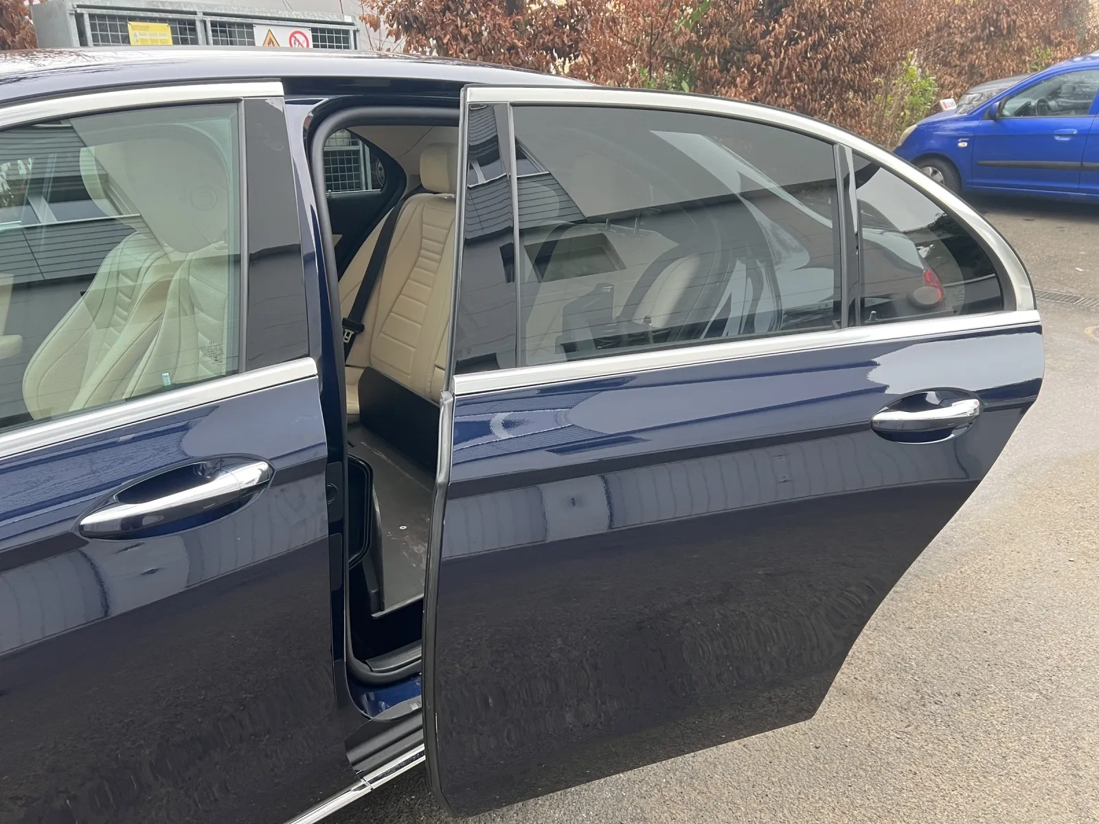 Dunkelblaue Limousine mit geöffneter Hintertür auf Parkplatz.