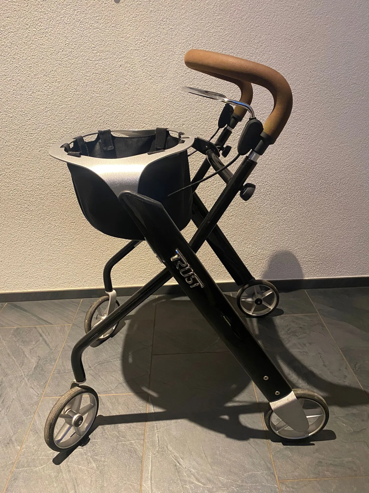 occasion-rollator-trust-weiss-02.jpg Zusammengeklappter Kinderwagen mit schwarzem Rahmen und braunem Griff.
