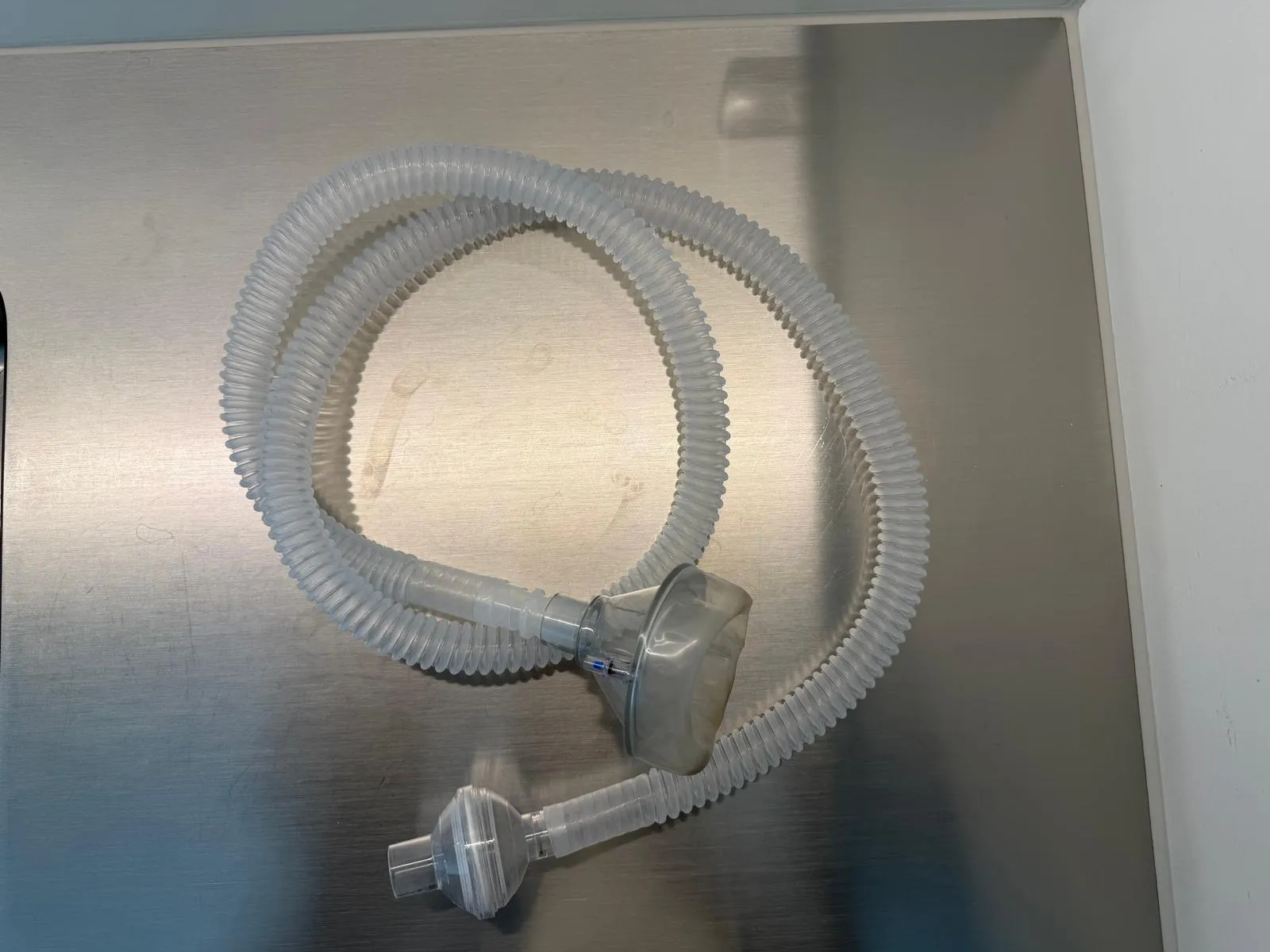 occasion-cough-assist-ofner-03.jpg Gewellter weißer Kunststoffschlauch mit Anschlüssen auf grauem Hintergrund.