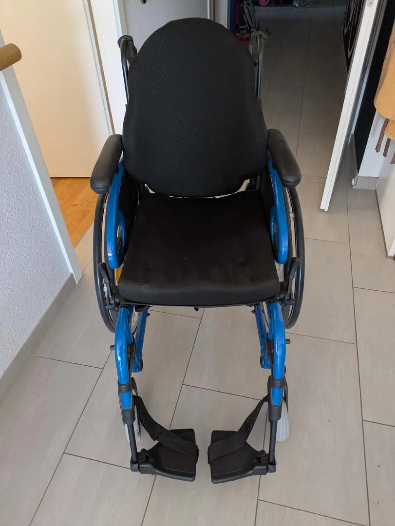 Schwarzer Rollstuhl mit blauem Rahmen auf weißen Fliesen.