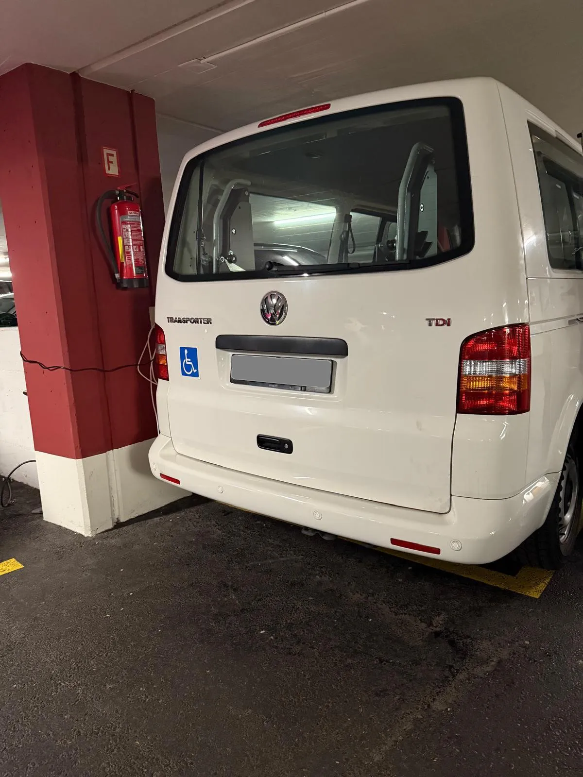 Weißer Transporter parkt neben roter Säule in Tiefgarage.