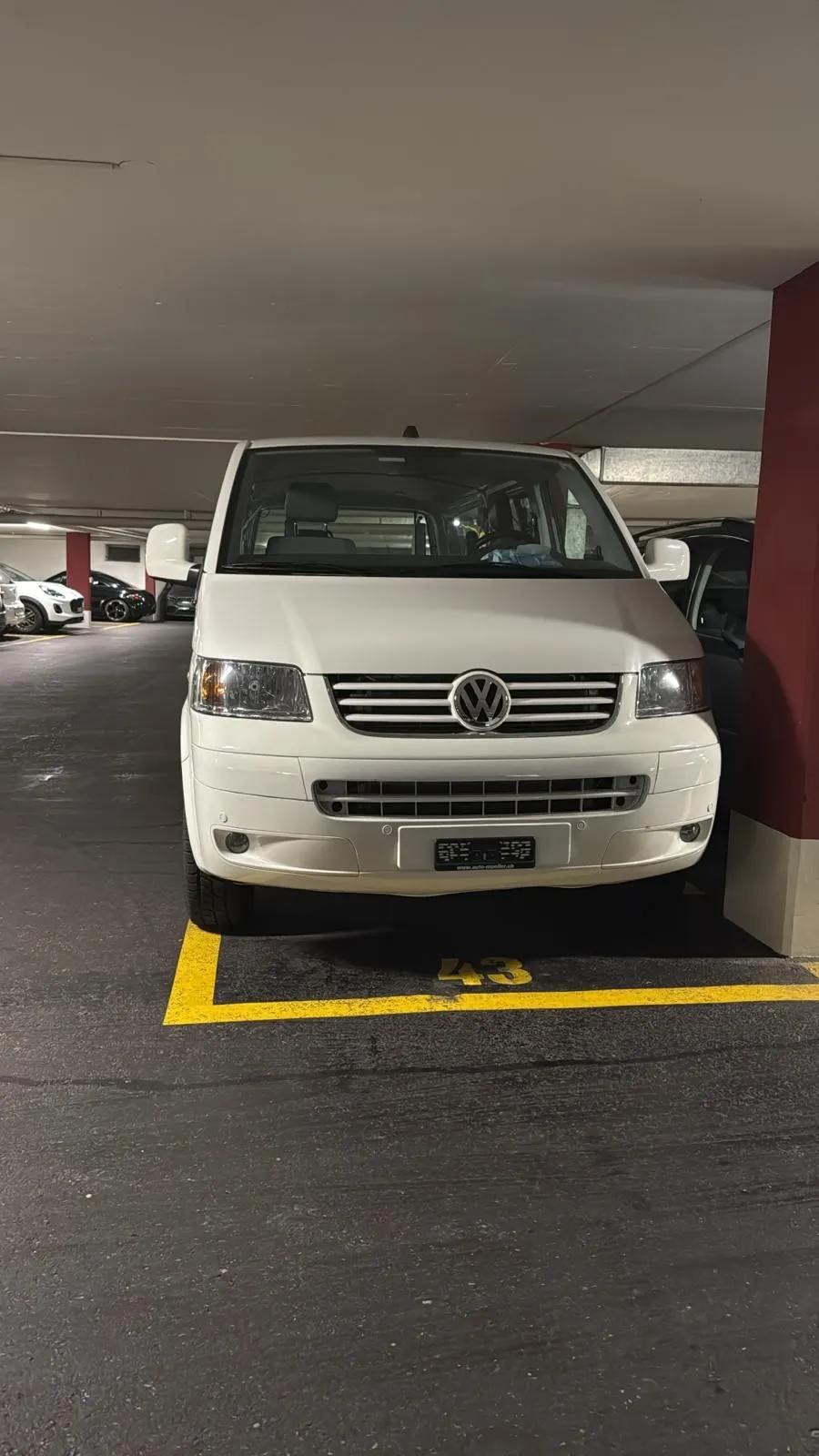 Weißer Volkswagen-Transporter in einem Parkhaus auf einem gelb markierten Parkplatz.