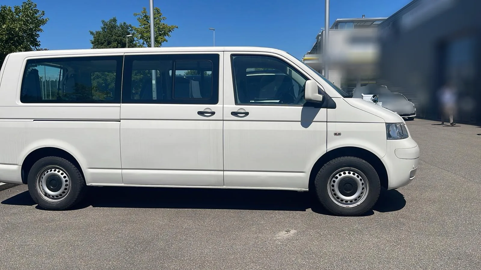 Weißer Volkswagen Transporter-Van parkt auf einem Parkplatz bei sonnigem Wetter.