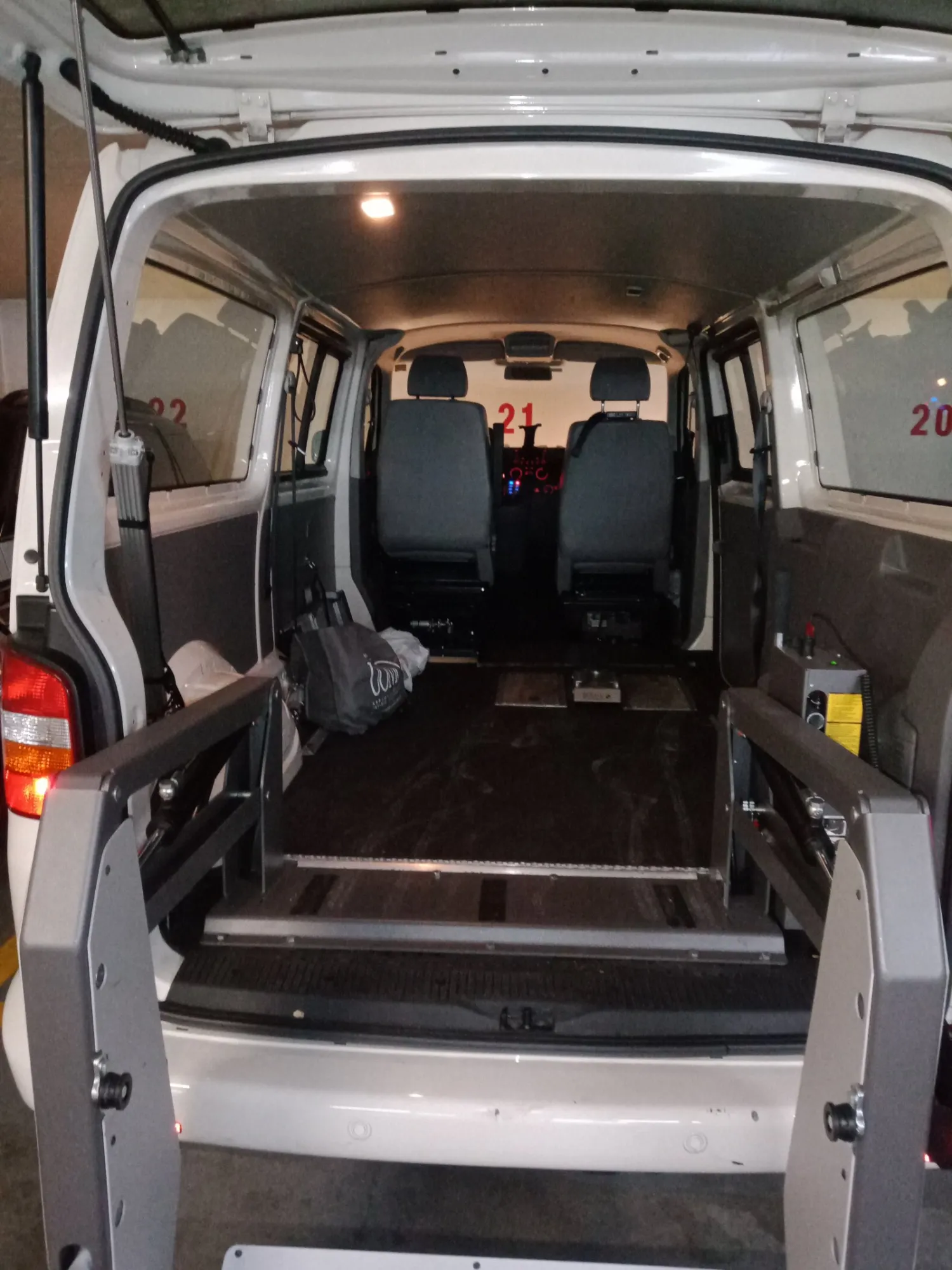 Innenansicht eines Transporters mit geöffneter Heckklappe, leerer Laderaum mit Sitzen und Rampe.