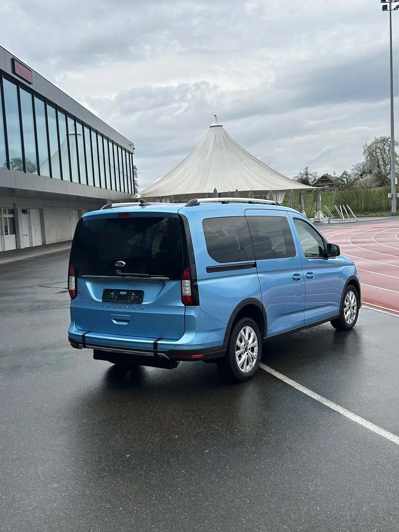 Blauer Volkswagen Caddy auf einem Parkplatz vor einem modernen Gebäude.
